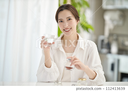 Woman drinking supplements in the living room Woman drinking supplements in the living room 112413639