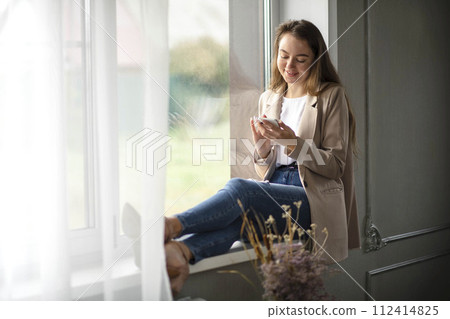 Work-life-balance, businesswoman on the windowsill in the office with smartphone 112414825