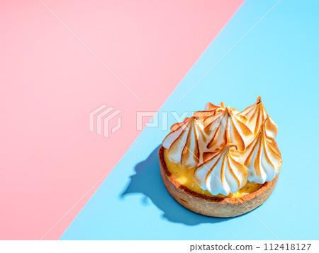 Mini cake decorated with whipped egg whites meringue. Mini lemon tart with burnt French meringue. Delicious dessert with lemon filling. topped with meringue on pink and blue, hard shadows, copy space Mini cake decorated with whipped egg whites meringue. Mini lemon tart with burnt French meringue. Delicious dessert with lemon filling. topped with meringue on pink and blue, hard shadows, copy space 112418127