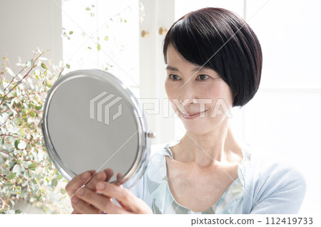 Beauty Woman holding a mirror by the window Beauty Woman holding a mirror by the window 112419733