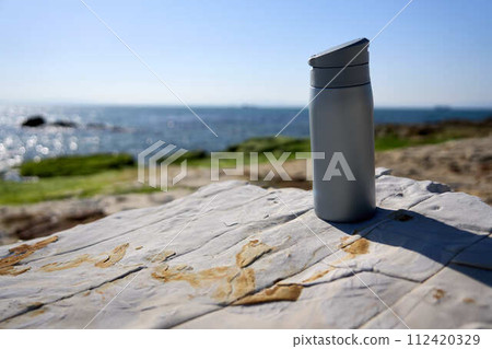 [Minamichita] A gray water bottle placed on a rocky area on the coast 112420329