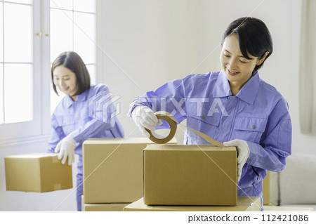 A female mover puts duct tape on cardboard with a smile 112421086