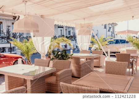 Wicker furniture tables in the open air are waiting for visitors. The interior of the restaurant in the open air. Empty tables of street cafe. Wicker furniture tables in the open air are waiting for visitors. The interior of the restaurant in the open air. Empty tables of street cafe. 112421228
