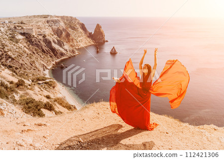 Woman red dress sea. Female dancer in a long red dress posing on a beach with rocks on sunny day. Girl on the nature on blue sky background. 112421306