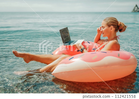 Woman laptop sea. Freelancer woman in sunglases floating on an inflatable big pink donut with a laptop in the sea. People summer vacation rest lifestyle concept 112421558