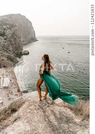 Woman sea trevel green dress. Side view a happy woman with long hair in a long mint dress posing on a beach with calm sea bokeh lights on sunny day. Girl on the nature on blue sky background. Woman sea trevel green dress. Side view a happy woman with long hair in a long mint dress posing on a beach with calm sea bokeh lights on sunny day. Girl on the nature on blue sky background. 112421633