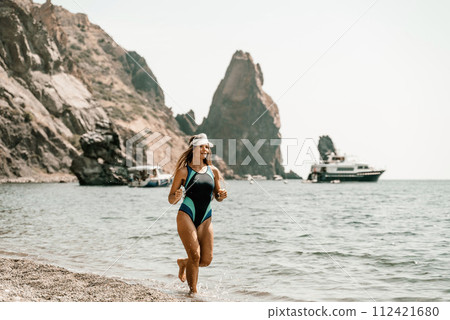Woman beach vacation photo. A happy tourist in a blue bikini enjoying the scenic view of the sea and volcanic mountains while taking pictures to capture the memories of her travel adventure. 112421680