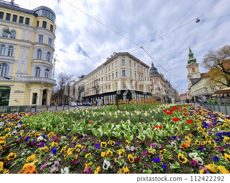 Graz, Austria - 26.03.2023: Colorful spring flowers in Jakominiplatz Square and Parish Church in the background, famous attraction in the city of Graz, Steiermark region, Austria. Selective focus Graz, Austria - 26.03.2023: Colorful spring flowers in Jakominiplatz Square and Parish Church in the background, famous attraction in the city of Graz, Steiermark region, Austria. Selective focus 112422292