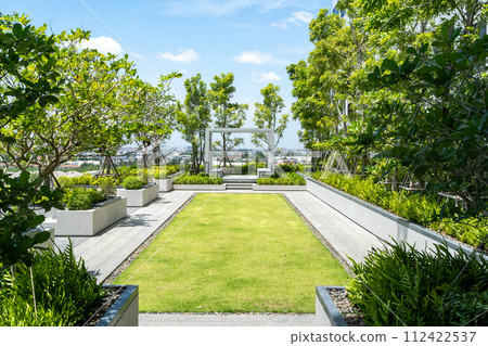 A neatly manicured rooftop garden pathway leading to a modern pergola with a panoramic city view.. 112422537