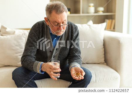 Middle aged senior man holding medical pill and glass of water. Mature old senior grandfather taking medication cure pills vitamin. Age prescription medicine healthcare therapy concept Middle aged senior man holding medical pill and glass of water. Mature old senior grandfather taking medication cure pills vitamin. Age prescription medicine healthcare therapy concept 112422657
