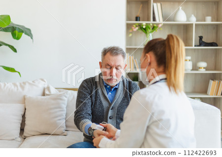 Female doctor senior man taking his blood pressure in doctor office or at home. Old man patient and doctor have consultation in hospital room. Medicine healthcare medical checkup. Visit to doctor 112422693