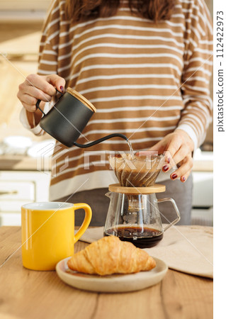 female makes coffee in morning kitchen. brews in purover. yellow cup with black coffee drip 112422973
