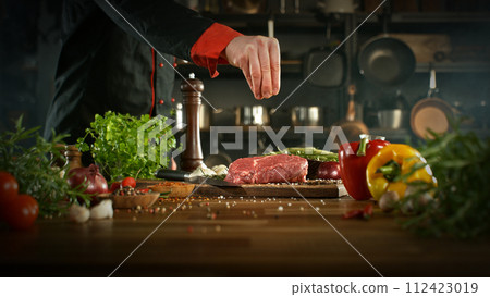 Close-up of falling salt on tasty beef steak in kitchen. Chef in background. 112423019
