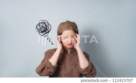 A woman wearing cooking clothes holding her head 112423707