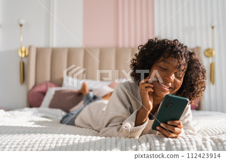 African girl holding smartphone touch screen typing scroll page at home. Woman with cell phone surfing internet using social media apps playing game. Shopping online Internet news cellphone addiction African girl holding smartphone touch screen typing scroll page at home. Woman with cell phone surfing internet using social media apps playing game. Shopping online Internet news cellphone addiction 112423914