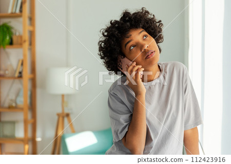 African american girl talking on smartphone at home indoor. Young woman with cell phone chatting with friends. Smiling teen girl making answering call by cellphone. Lady having conversation by mobile African american girl talking on smartphone at home indoor. Young woman with cell phone chatting with friends. Smiling teen girl making answering call by cellphone. Lady having conversation by mobile 112423916