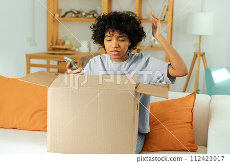Unhappy african woman unpack delivered box receiving damaged shipping problem in postal service. Annoyed confused customer receiving wrong parcel talks to customers support. Bad delivery services Unhappy african woman unpack delivered box receiving damaged shipping problem in postal service. Annoyed confused customer receiving wrong parcel talks to customers support. Bad delivery services 112423917