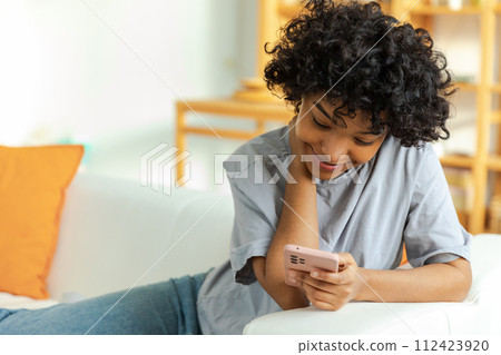 African girl holding smartphone touch screen typing scroll page at home. Woman with cell phone surfing internet using social media apps playing game. Shopping online Internet news cellphone addiction 112423920