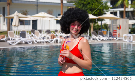 The girl enjoys sunbathing by the pool and drinks a cocktail The girl enjoys sunbathing by the pool and drinks a cocktail 112424565