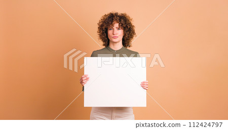 Happy woman holding blank paper in beige studio Happy woman holding blank paper in beige studio 112424797