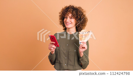 Excited woman with cash and looking phone in beige studio Excited woman with cash and looking phone in beige studio 112424798