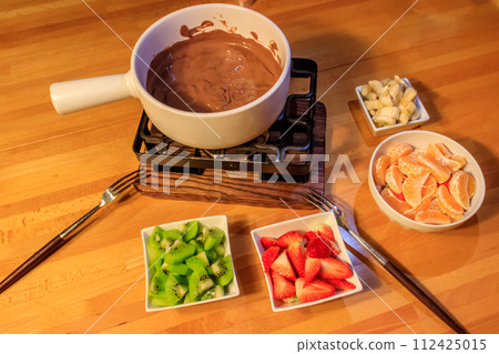 Chocolate fondue with fruits on wooden table. Cooking fondue 112425015