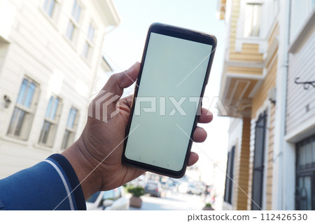 young man hand using smart phone with empty screen against city buildings  112426530