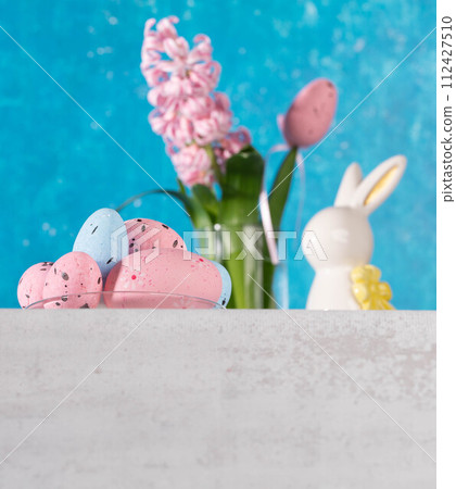 Eggs, ceramic bunny, pink jacinth on white table. Turquoise backdrop. Easter card. Low angle shot. Eggs, ceramic bunny, pink jacinth on white table. Turquoise backdrop. Easter card. Low angle shot. 112427510