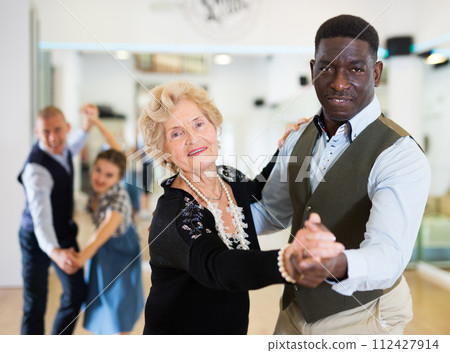 Elderly woman learning ballroom dancing in pair in dance studio Elderly woman learning ballroom dancing in pair in dance studio 112427914