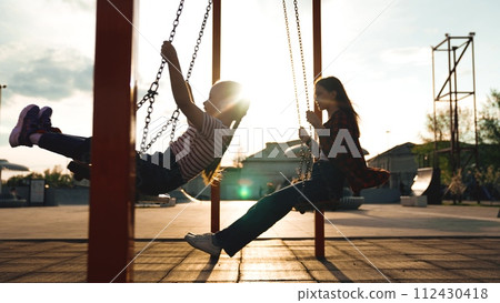Happy female children silhouette swinging swing at summer sunset sunrise sky outdoor sport playground. Girl kids adolescent having fun flying enjoy leisure activity childhood recreation joyful playing 112430418