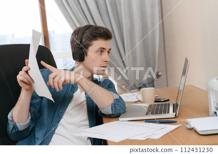 Serious handsome guy works remotely using laptop for video call 112431230