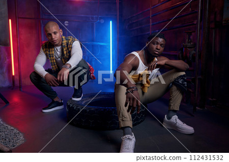 Two young drug dealers with serious faces posing for camera in neon light Two young drug dealers with serious faces posing for camera in neon light 112431532