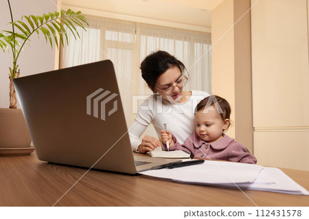 positive businesswoman in glasses working on laptop at home with her little child girl. Stay at home 112431578