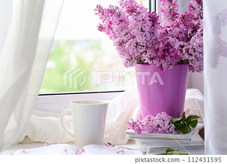The postcard is beautiful. A mug of tea, an old book and a bouquet of purple lilac. A beautiful still life. Spring time. The concept of Good morning. The postcard is beautiful. A mug of tea, an old book and a bouquet of purple lilac. A beautiful still life. Spring time. The concept of Good morning. 112431595