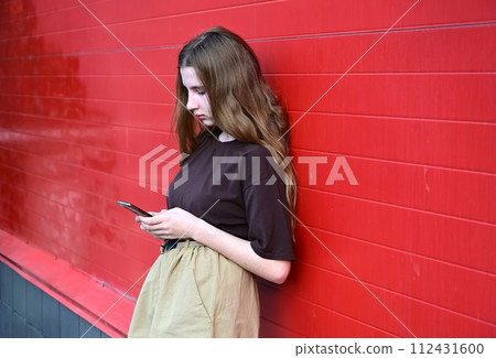 Portrait of a young student reading a message on a mobile phone, a stylish pretty girl chatting on a mobile phone while walking down the street disorder, disorder, technology, disease,dependent 112431600