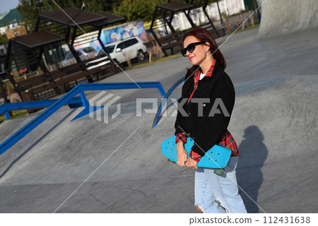 An active middle-aged woman rides a skateboard on an empty road or highway. An ordinary city woman relaxing on a skateboard after work. The concept of a modern lifestyle 112431638