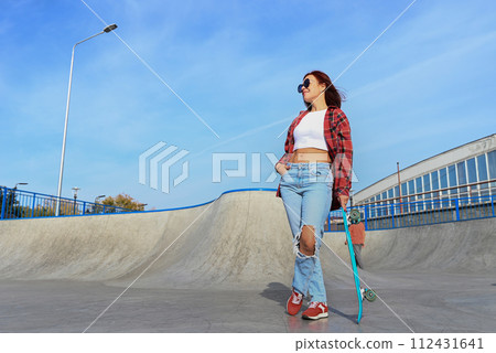 An active middle-aged woman rides a skateboard on an empty road or highway. An ordinary city woman relaxing on a skateboard after work. The concept of a modern lifestyle 112431641