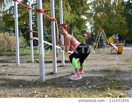 An athlete in comfortable sportswear. Outdoor fitness in the city. Healthy lifestyle. Coach exercises on the street. A confident woman does a workout. An athlete in comfortable sportswear. Outdoor fitness in the city. Healthy lifestyle. Coach exercises on the street. A confident woman does a workout. 112431850