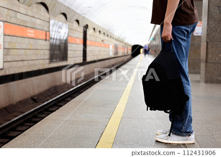 a girl with a backpack is waiting for a train at the station 112431906