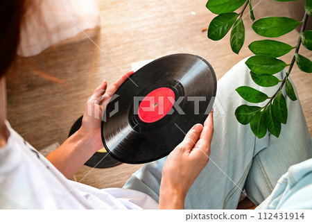 Vinyl records on a wooden table. The girl's hand examines vinyl records. Retro style. Sound technology for DJ to mix and play music. Black vinyl record. Vinyl records on a wooden table. The girl's hand examines vinyl records. Retro style. Sound technology for DJ to mix and play music. Black vinyl record. 112431914
