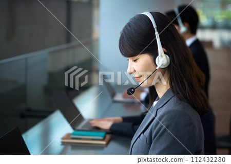 一位穿著西裝的女商人在辦公室裡戴著耳機並做出回應 一位穿著西裝的女商人在辦公室裡戴著耳機並做出回應 112432280