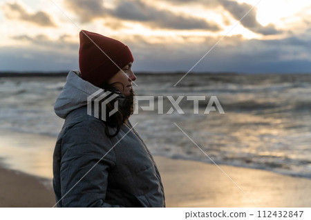 a woman stands on the seashore in the cold during a storm.  112432847