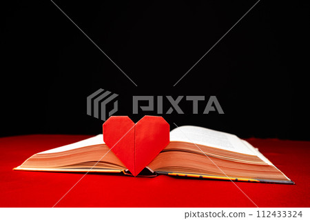 Origami paper heart and thick book on red and black background. Love for books. Origami paper heart and thick book on red and black background. Love for books. 112433324