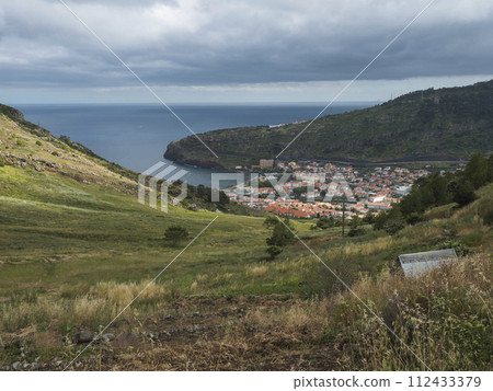 Aerial view on Machico town from Levada do Canical hiking trail. Footpath in green hills and tropical vegetation on Madeira island, Portugal, Europe. Aerial view on Machico town from Levada do Canical hiking trail. Footpath in green hills and tropical vegetation on Madeira island, Portugal, Europe. 112433379