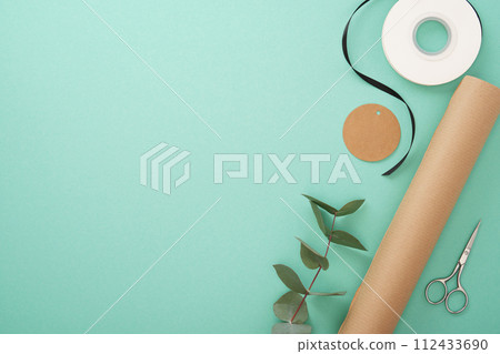 Gift wrapping. Brown craft wrapping paper, black ribbon, scissors, eucalyptus, tags. Mint background. Copyspace 112433690