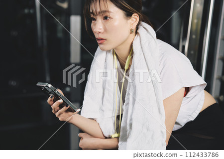 在健身房使用智慧型手機的女性 在健身房使用智慧型手機的女性 112433786