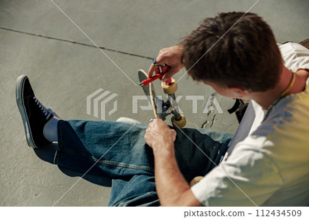 View of a man repairing his skateboard in the skate park. Extreme sport concept 112434509