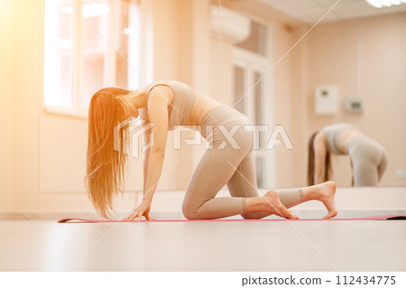 Girl does yoga. Young woman practices asanas on a beige one ton background. Girl does yoga. Young woman practices asanas on a beige one ton background. 112434775