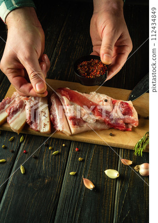 A man seasones lard with spices on a wooden cutting board. The concept of preparing delicious peasant lard with garlic for an appetizer 112434849