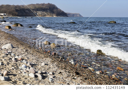 The sea wave beats against a stone on the shore. Blue sea and rocky shore The sea wave beats against a stone on the shore. Blue sea and rocky shore 112435149